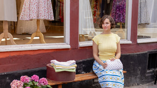 Woman sitting on a bench in front of a store with clothing displayed.